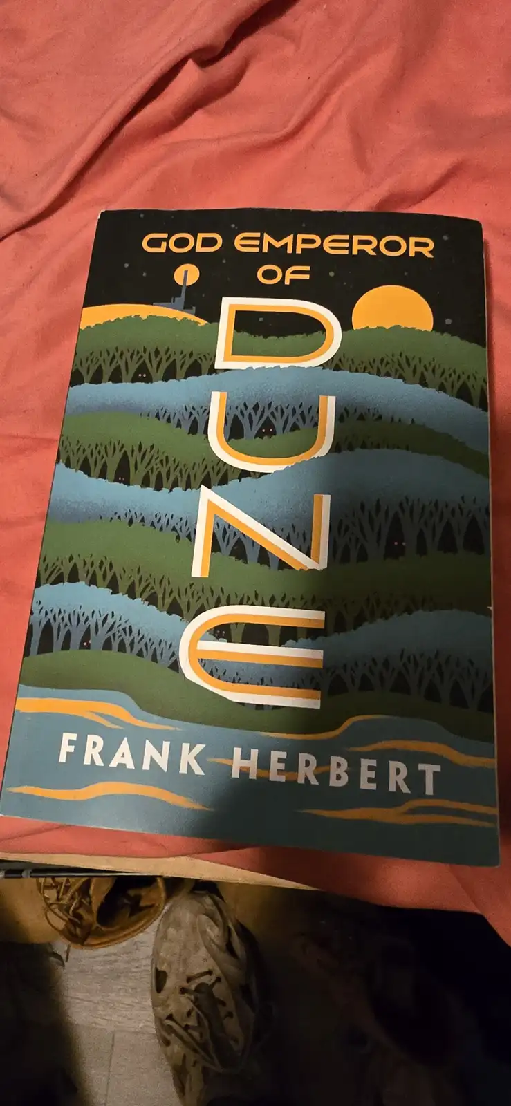 A physical copy of Frank Herbert's 'God Emperor of Dune' book lies on a red fabric surface, with the cover art showing…
