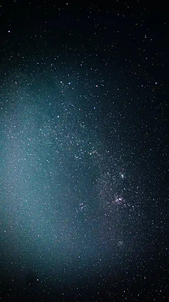 A vertical photograph of a starry night sky with a teal and black gradient, featuring countless stars and faint nebulae…