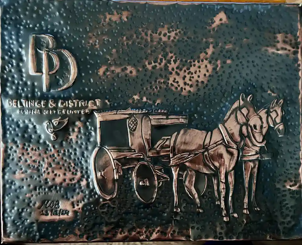 A textured, metallic plaque features an embossed image of a horse-drawn hearse with two horses, alongside the text 'BELTINGE…