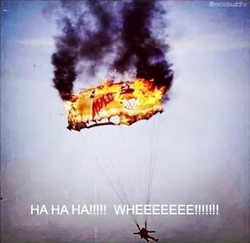 A parachutist is falling with a burning, charred parachute emitting thick black smoke above them. The parachutist is…