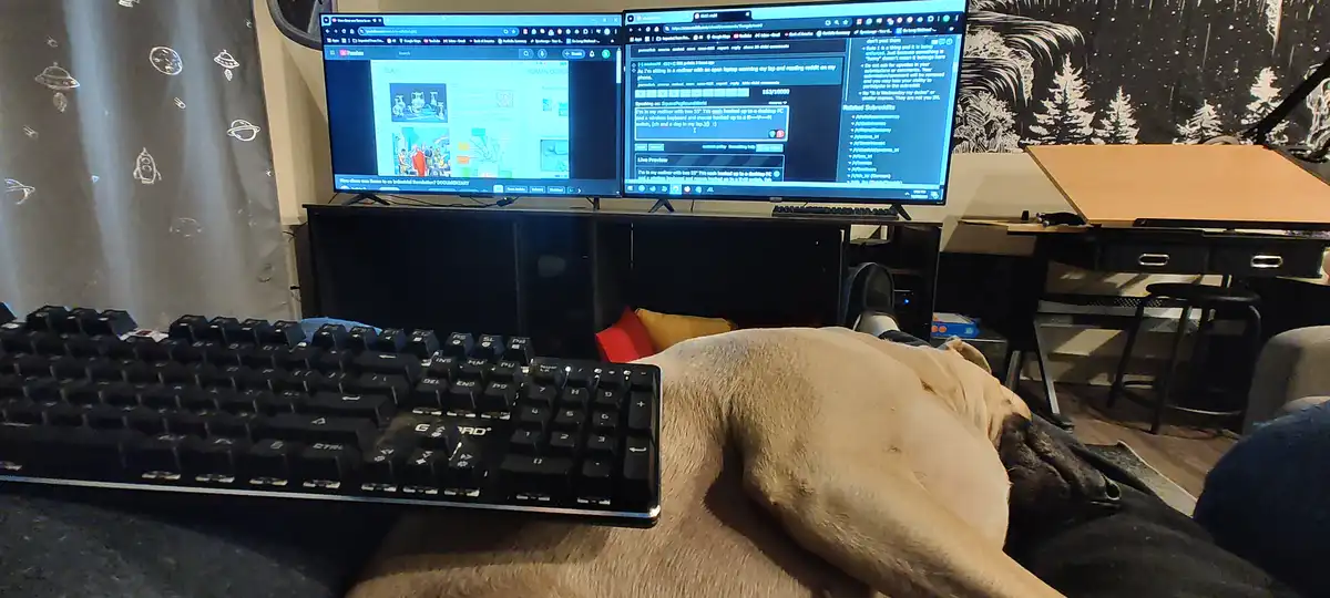 A person is lounging in a recliner with a large, light-brown dog resting on their lap, partially obscuring a black keyboard…