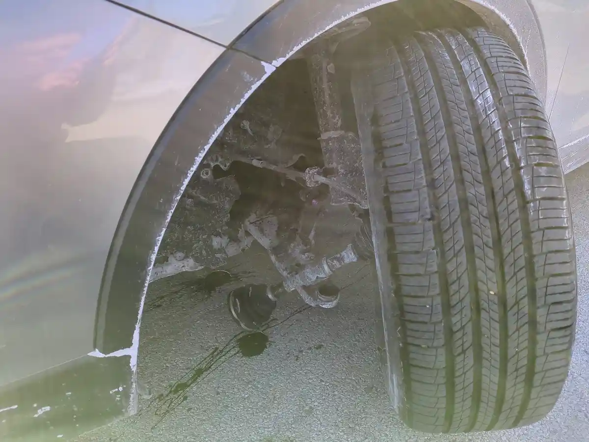 A close-up photo shows a car's wheel well and tire covered in a thick layer of ice, with the car's body and ground also icy…