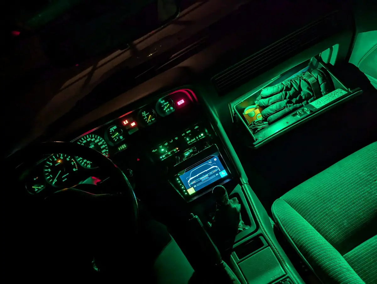 A dimly lit car interior bathed in green ambient lighting, showing the dashboard with glowing gauges, a modern touchscreen…