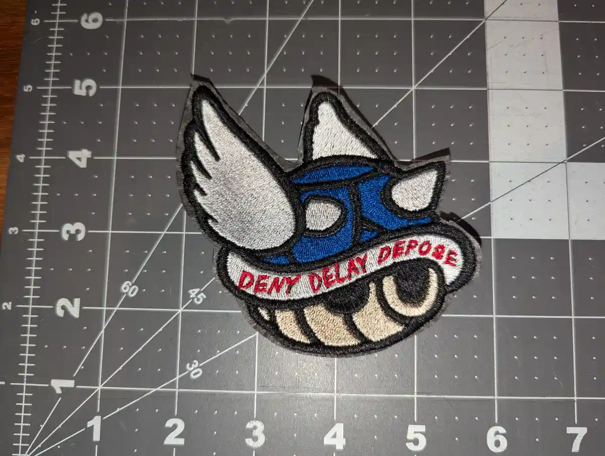 An embroidered patch depicting a stylized, cartoonish fox-like creature with blue face, white ears, and a wide grin showing…