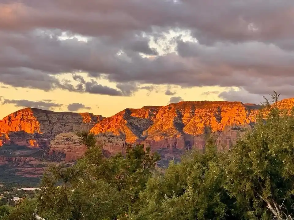 A scenic photo of a mountain range at sunset, with orange and red rock formations illuminated by the low sun, partially…