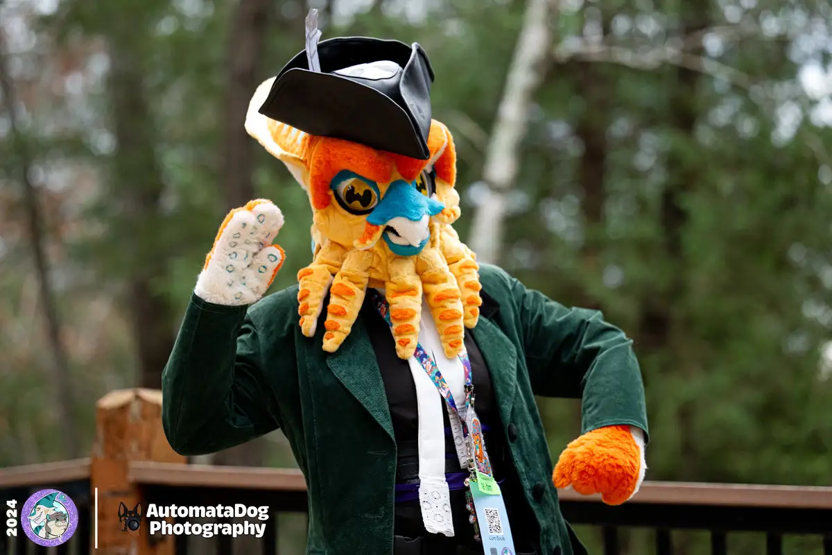 A person in a detailed orange and yellow octopus fursuit with a black pirate hat and feather, wearing a green velvet coat…