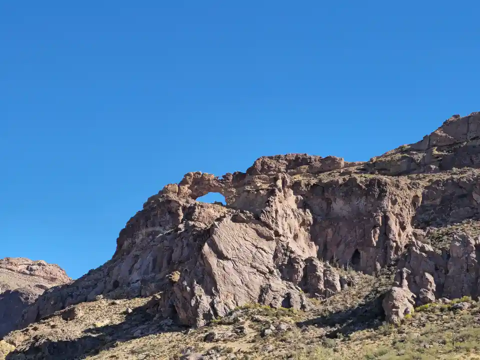 A natural rock arch formation in a desert landscape under a clear blue sky, with overlaid text reading 'i'm not a fan of the…