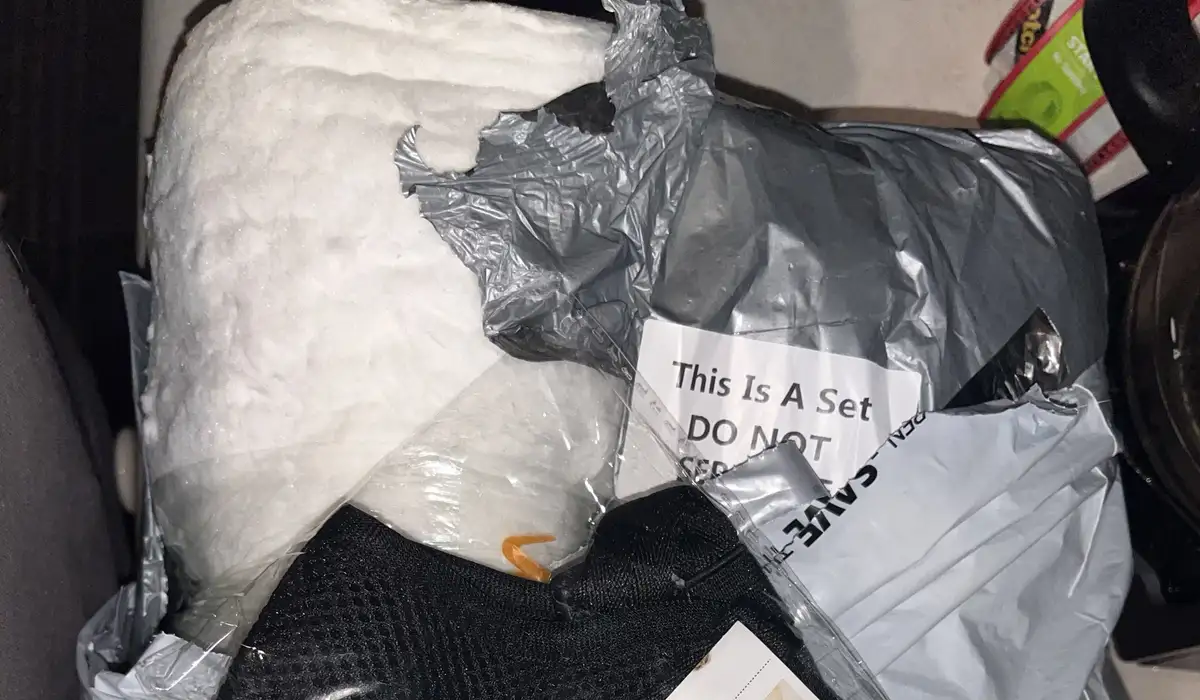 A pile of unopened, wrapped items including bubble wrap, plastic bags, and a black mesh bag, with a white paper label that…