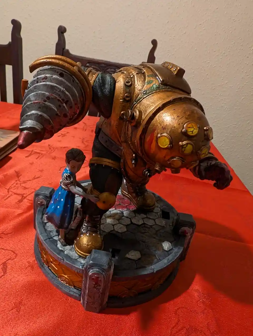 A figurine of a large, armored, steampunk-style robot with a drill arm and glowing yellow eyes stands on a circular base. A…