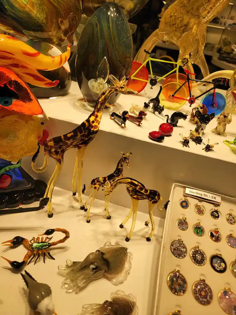 A display of colorful glass art including giraffes, dogs, cats, a bicycle, and insects, next to a tray labeled 'Sterling…