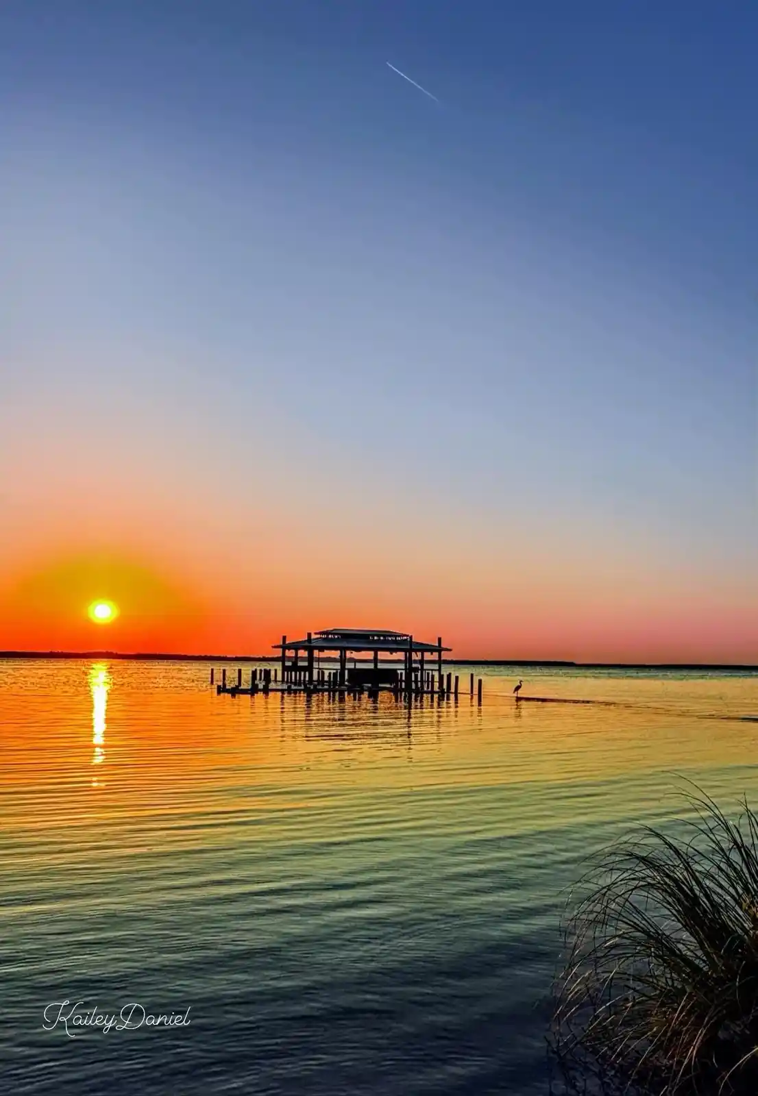 A serene sunset over water with a dock and a bird in silhouette, overlaid with the text 'i'm not lazy, i'm just conserving…