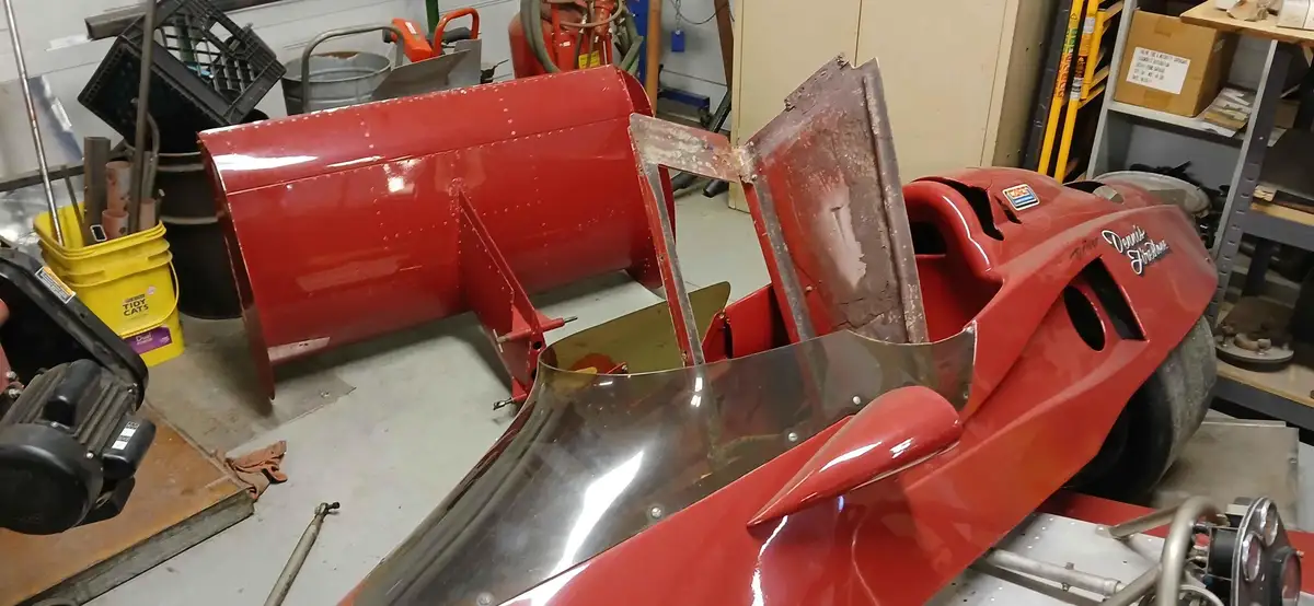 A red race car body in a workshop, with its side panel ripped open and the interior exposed, revealing a partially assembled…