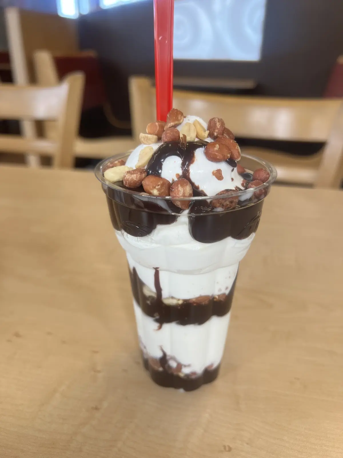A tall, clear plastic cup filled with alternating layers of white whipped cream and dark chocolate syrup, topped with a…