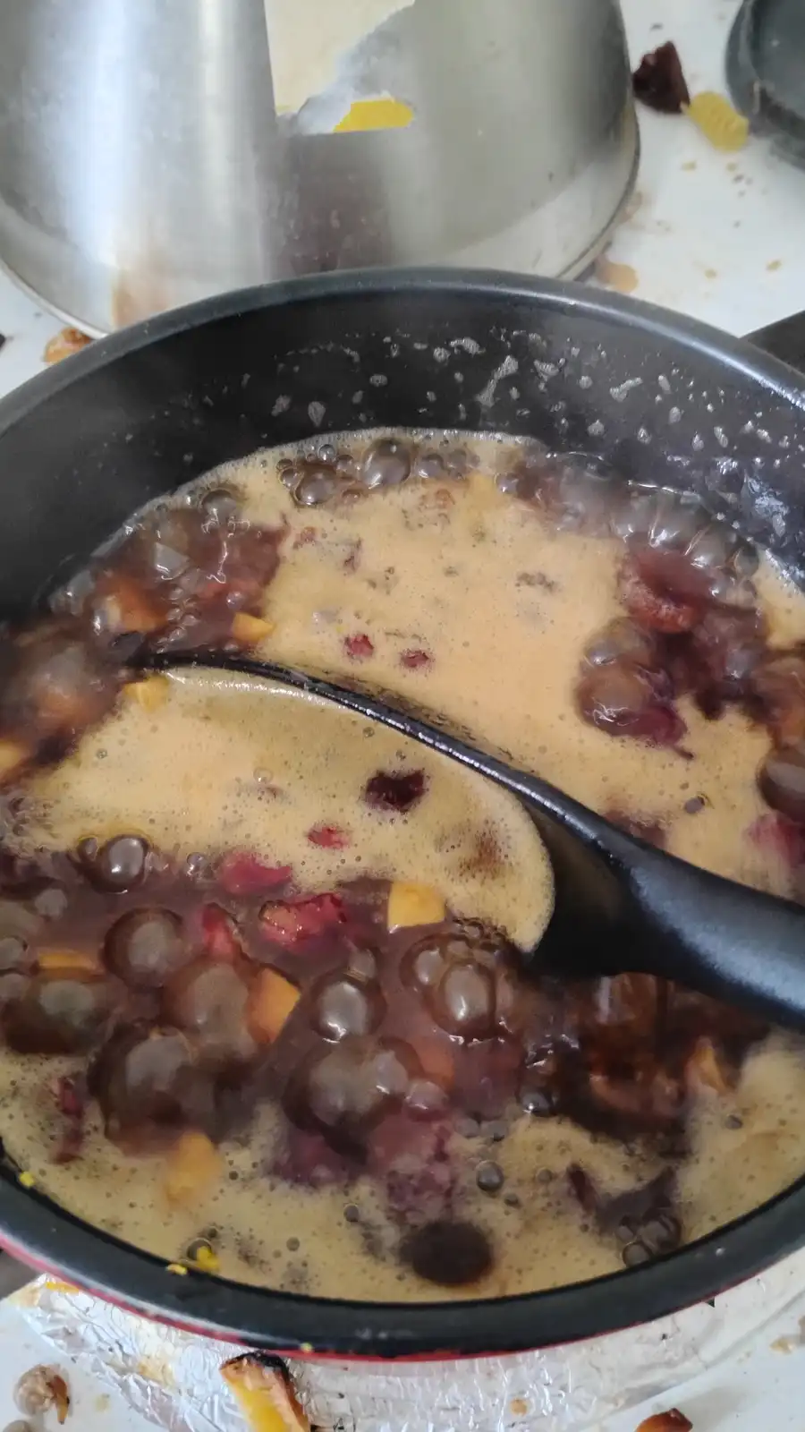 A close-up photo shows a black pot filled with a bubbling, dark brown liquid containing translucent tapioca pearls, red…