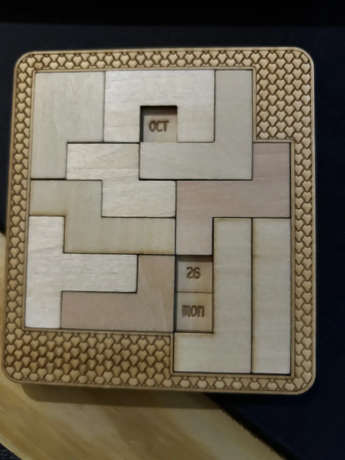 A wooden puzzle calendar with interlocking pieces forming a grid, where the top-center piece reads 'OCT' and the…