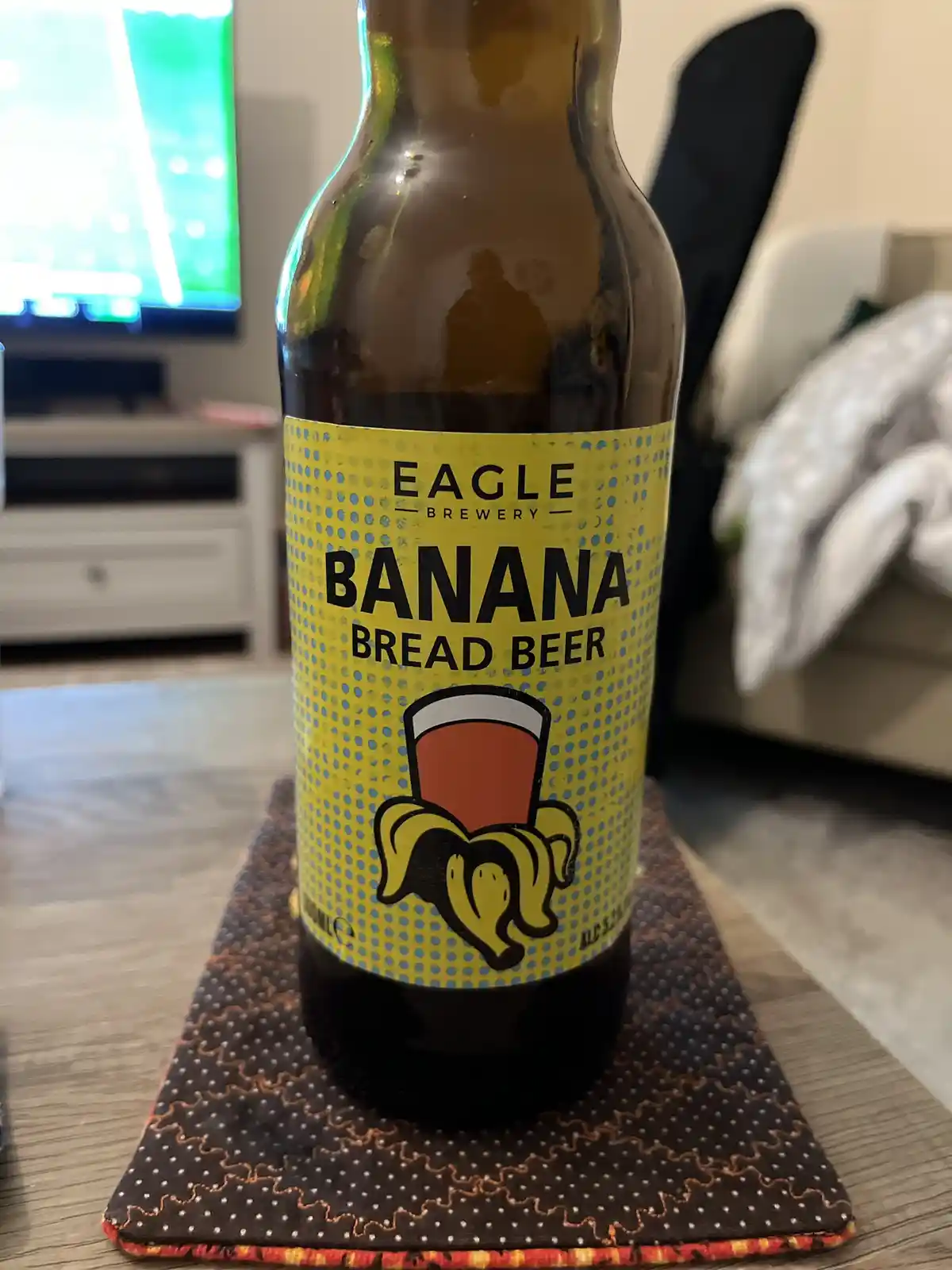 A close-up photo of a brown glass beer bottle with a bright yellow label from Eagle Brewery that reads 'BANANA BREAD BEER'…