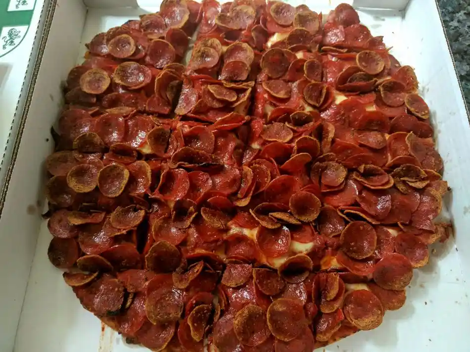 A close-up photo of a pepperoni pizza in an open cardboard box, with the pepperoni slices arranged in a way that visually…
