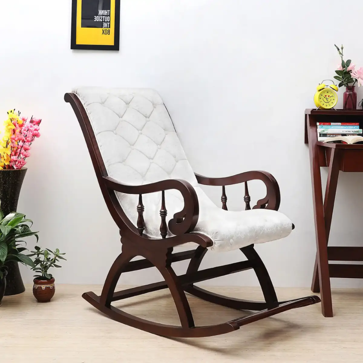 A dark wood rocking chair with white tufted upholstery sits in a staged room with a small side table holding a yellow…