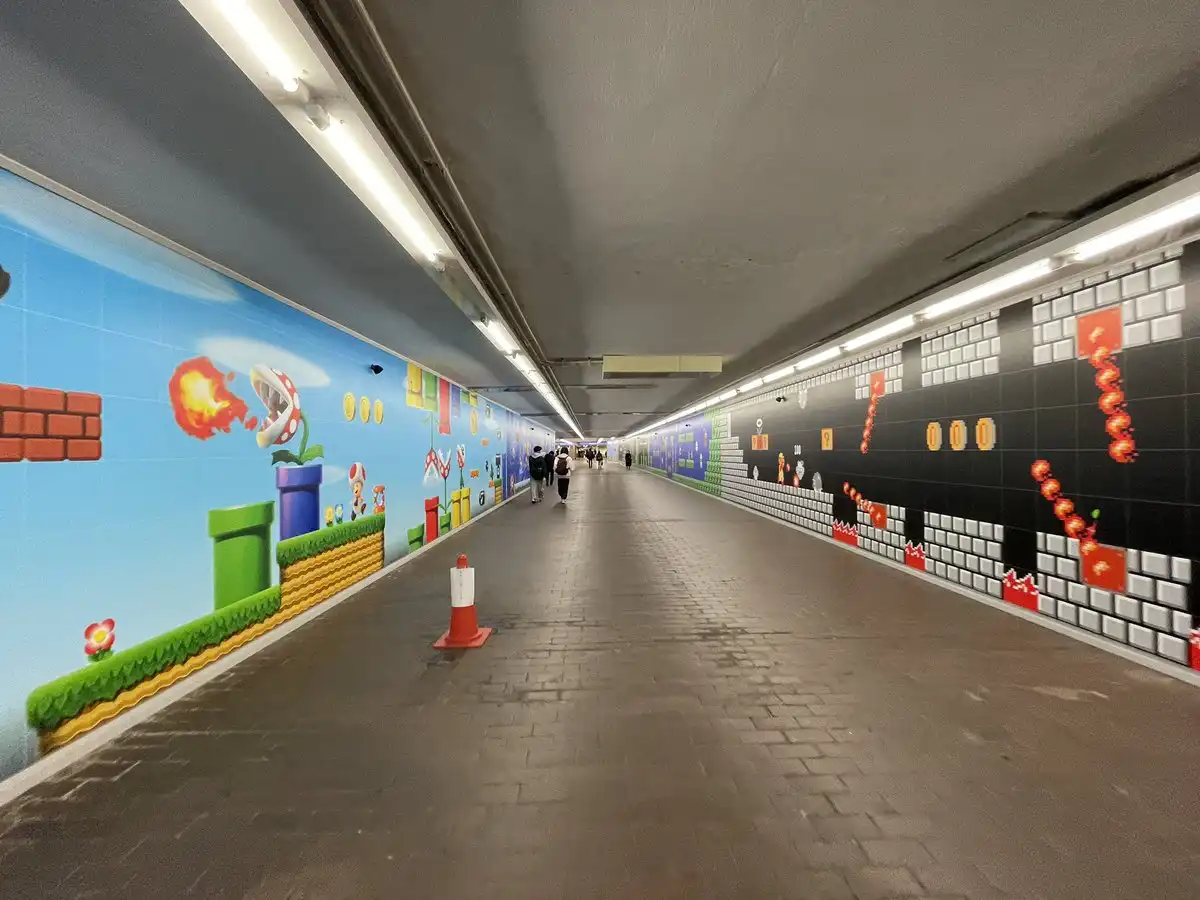 a long, real-world pedestrian tunnel is entirely decorated with vibrant, pixelated Super Mario Bros. video game wall murals…