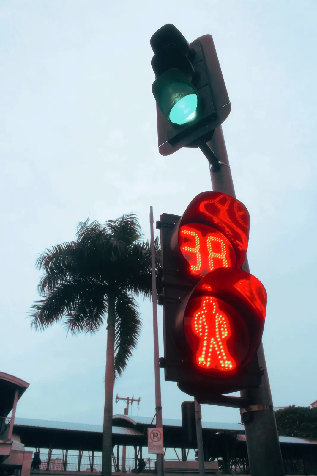 A low-angle photo shows a traffic light pole with a green light illuminated at the top and a red pedestrian signal below…