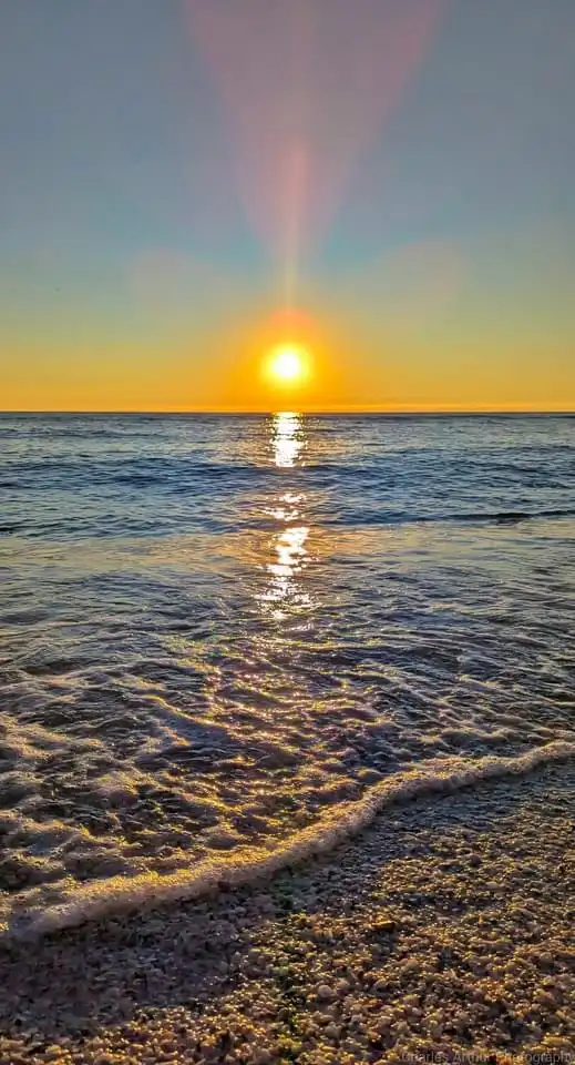 A serene sunset over the ocean with the sun low on the horizon, casting a golden reflection on the water and illuminating…