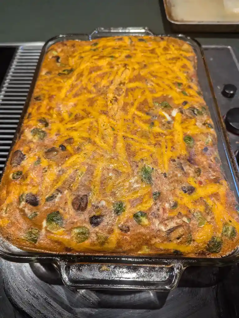 A close-up photo shows a rectangular glass baking dish filled with a golden-brown casserole topped with melted orange…
