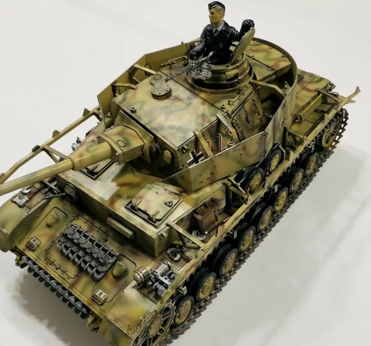 A highly detailed scale model of a German World War II tank, painted in camouflage with a crew figure seated in the open…