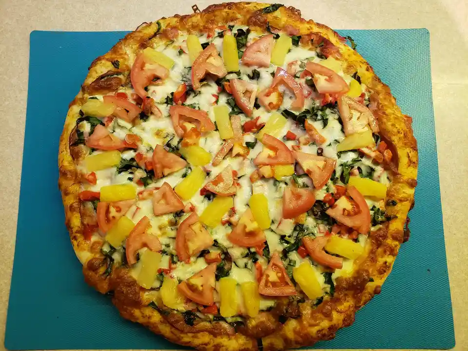 A freshly baked pizza with a golden crust sits on a blue cutting board, topped with melted cheese, chunks of red tomato, and…