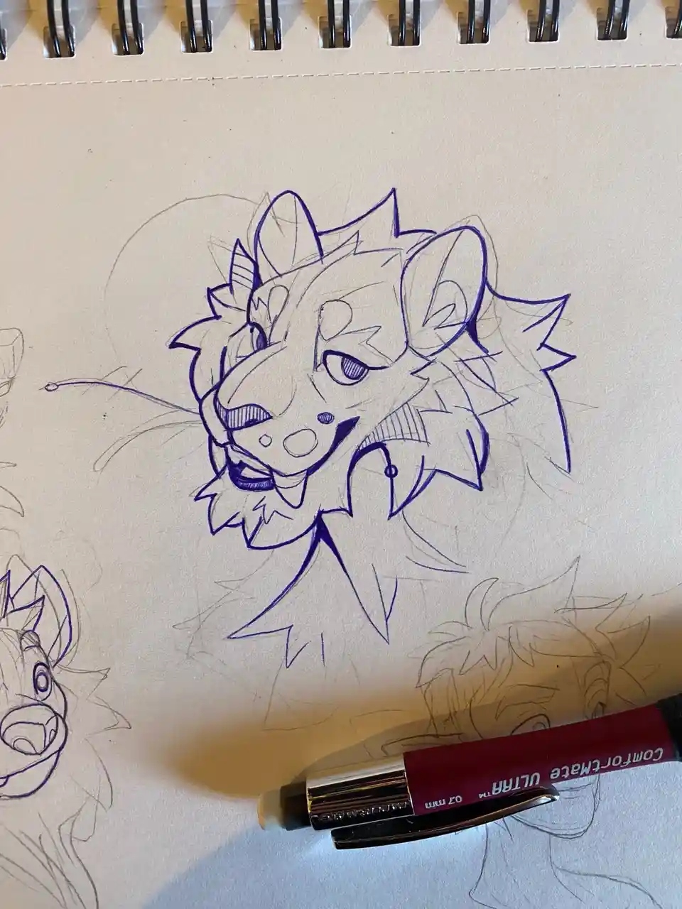 A close-up photo of a sketchbook page showing a blue ink drawing of an anthropomorphic feline character with spiky hair and…