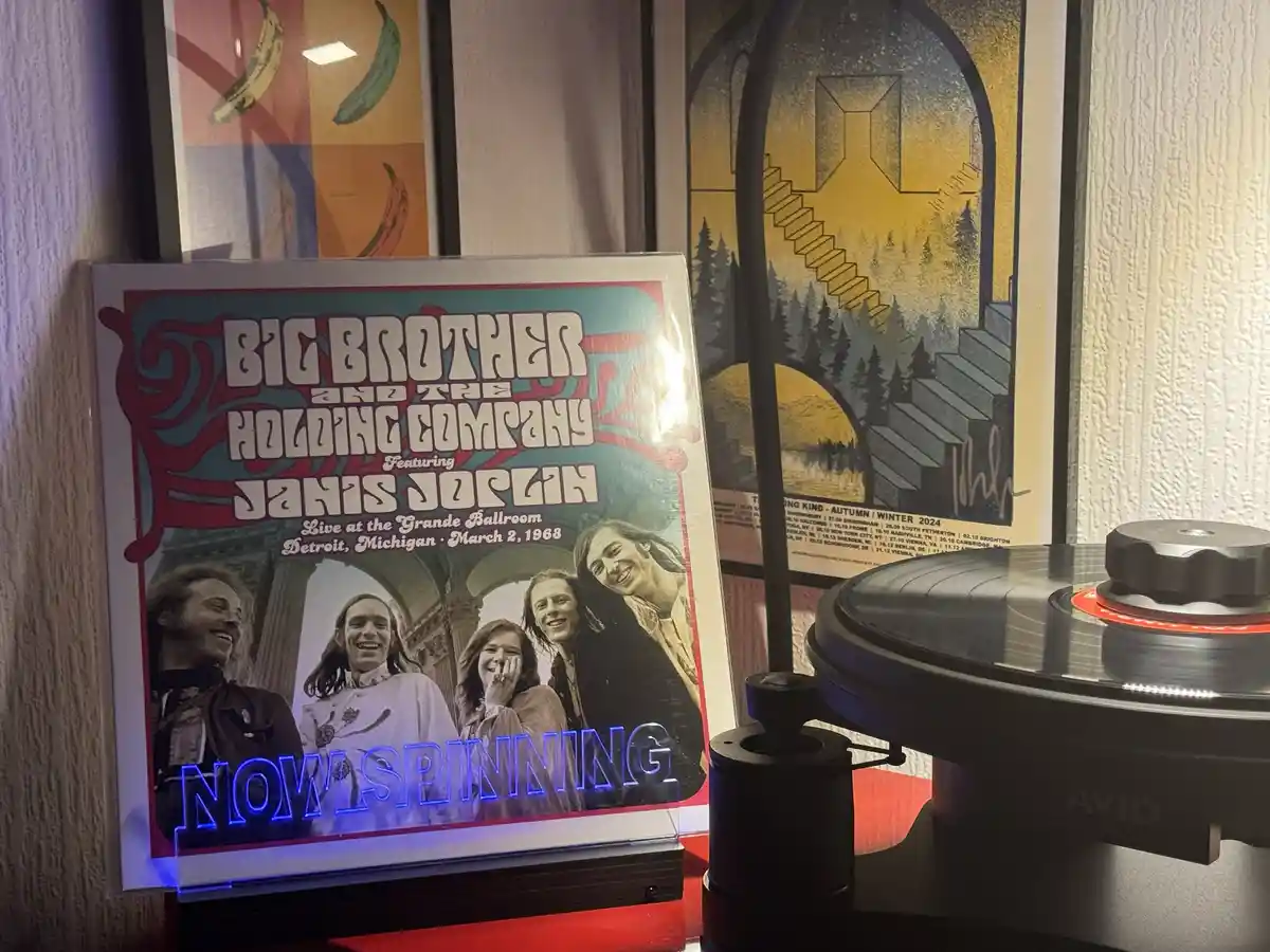 A vinyl record player with a spinning record sits next to a framed album cover for 'Big Brother and the Holding Company…
