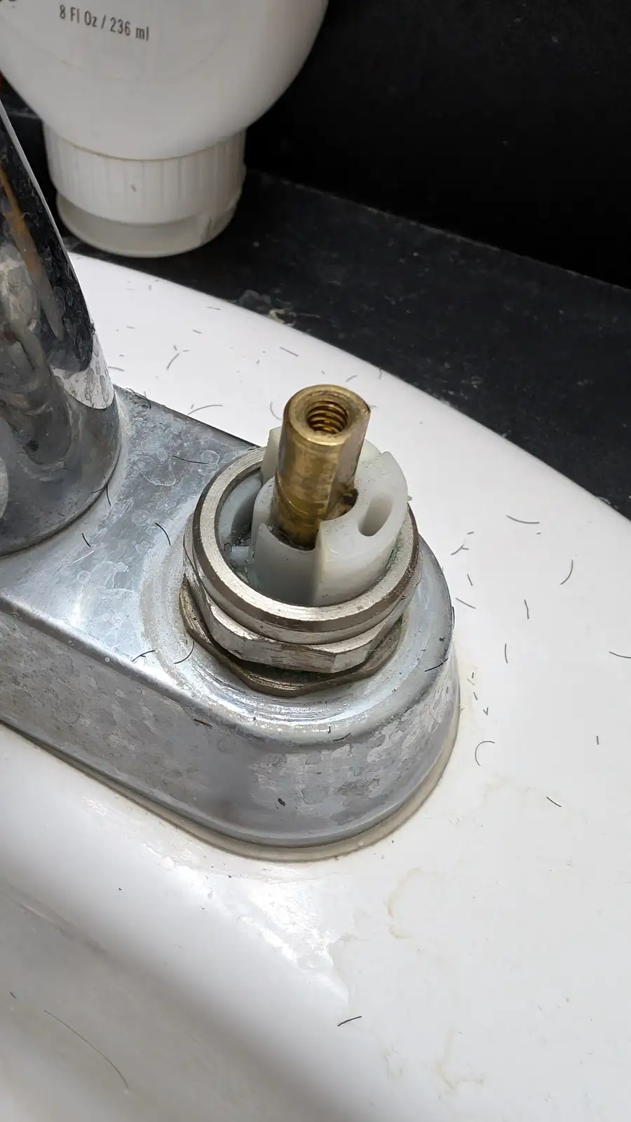 A close-up photo shows the exposed internal mechanism of a faucet, with a brass valve stem and white plastic washer visible…