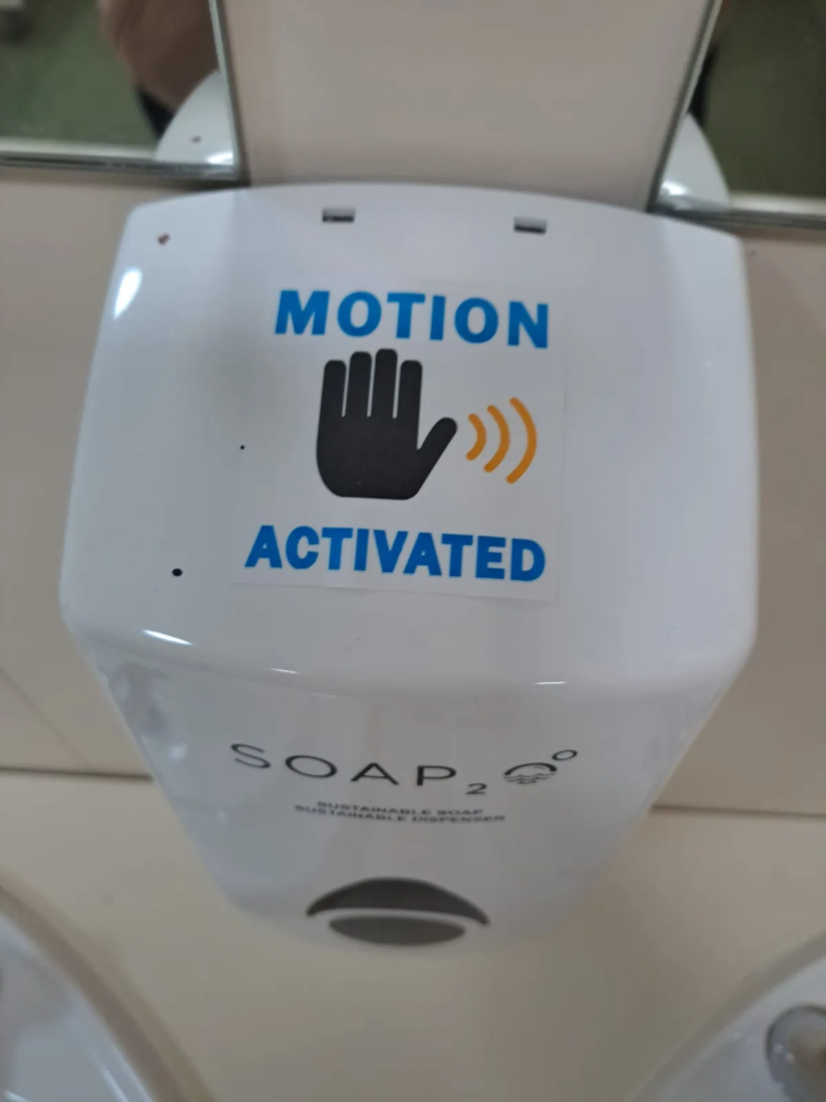 A close-up of a white automatic soap dispenser labeled 'SOAP₂' with a sticker that reads 'MOTION ACTIVATED' above a black…