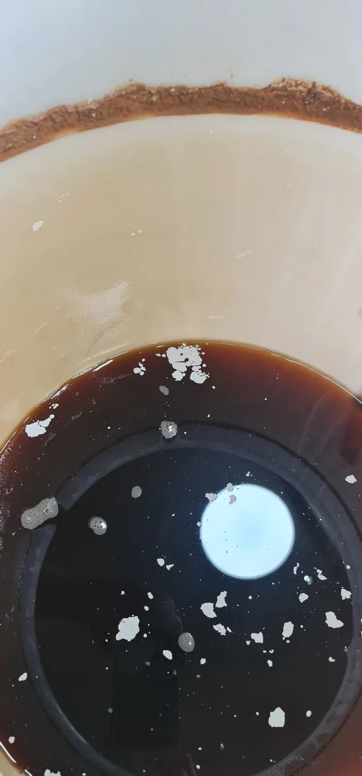 A top-down view of a coffee cup showing a dark coffee layer at the bottom and a lighter, creamy layer above it, with white…