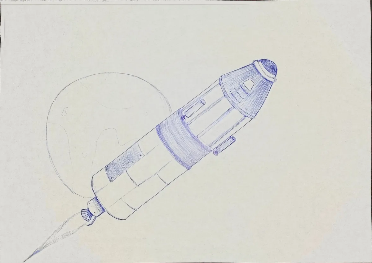 A blue pencil sketch on white paper shows a rocket with a pointed nose cone and exhaust plume, angled toward a simple…