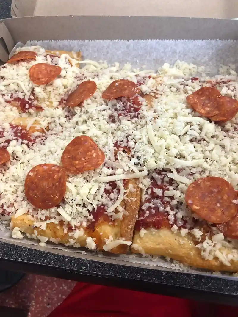 A close-up photo of a rectangular pizza in a cardboard box, covered in tomato sauce, shredded white cheese, and pepperoni…