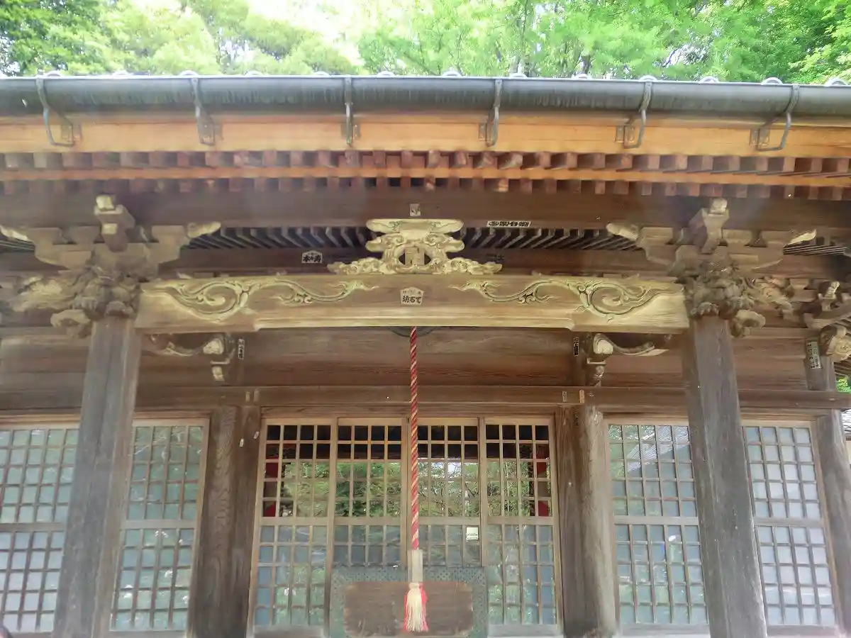 A close-up photograph of a traditional Japanese shrine's wooden entrance, featuring ornate carvings, a red-and-white rope…