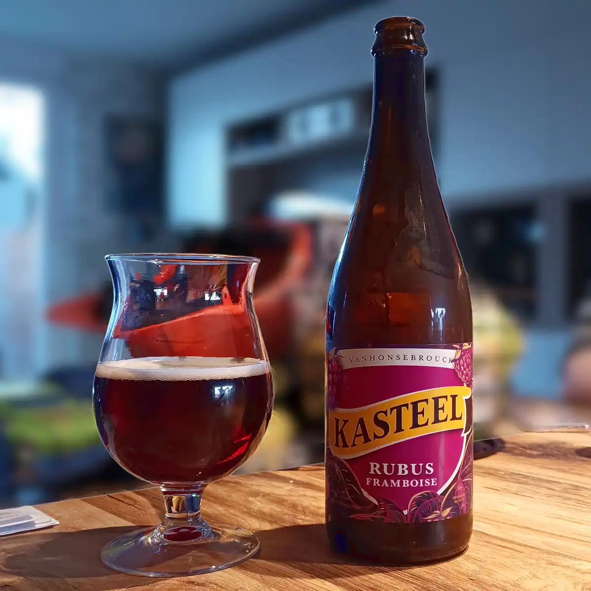 A bottle of Vanhonsebrouck Kasteel Rubus Framboise beer sits next to a tulip glass filled with the dark red beverage and a…