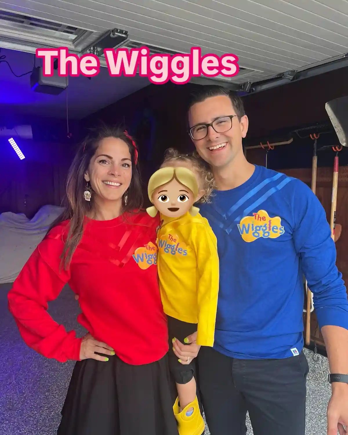 A family of three—a woman in a red shirt, a man in a blue shirt, and a child in a yellow shirt—all wearing 'The Wiggles'…