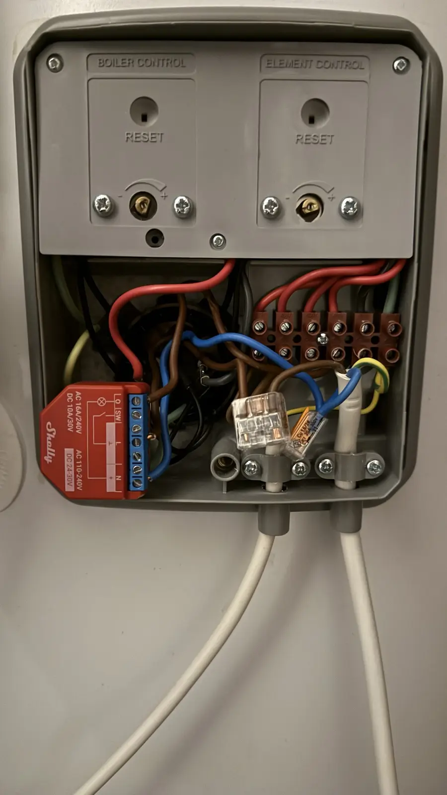A close-up photo of an open electrical control panel for a boiler and heating element, showing two 'RESET' buttons labeled…