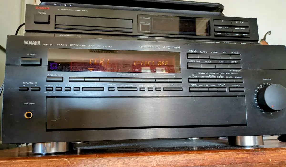 A close-up of a black Yamaha stereo receiver with a digital display showing 'VCR 1 EFFECT OFF' in orange text. Above it sits…
