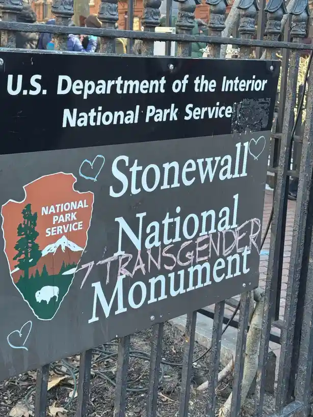 A National Park Service sign for Stonewall National Monument is shown with pink graffiti that reads 'TRANSGENDER' over the…