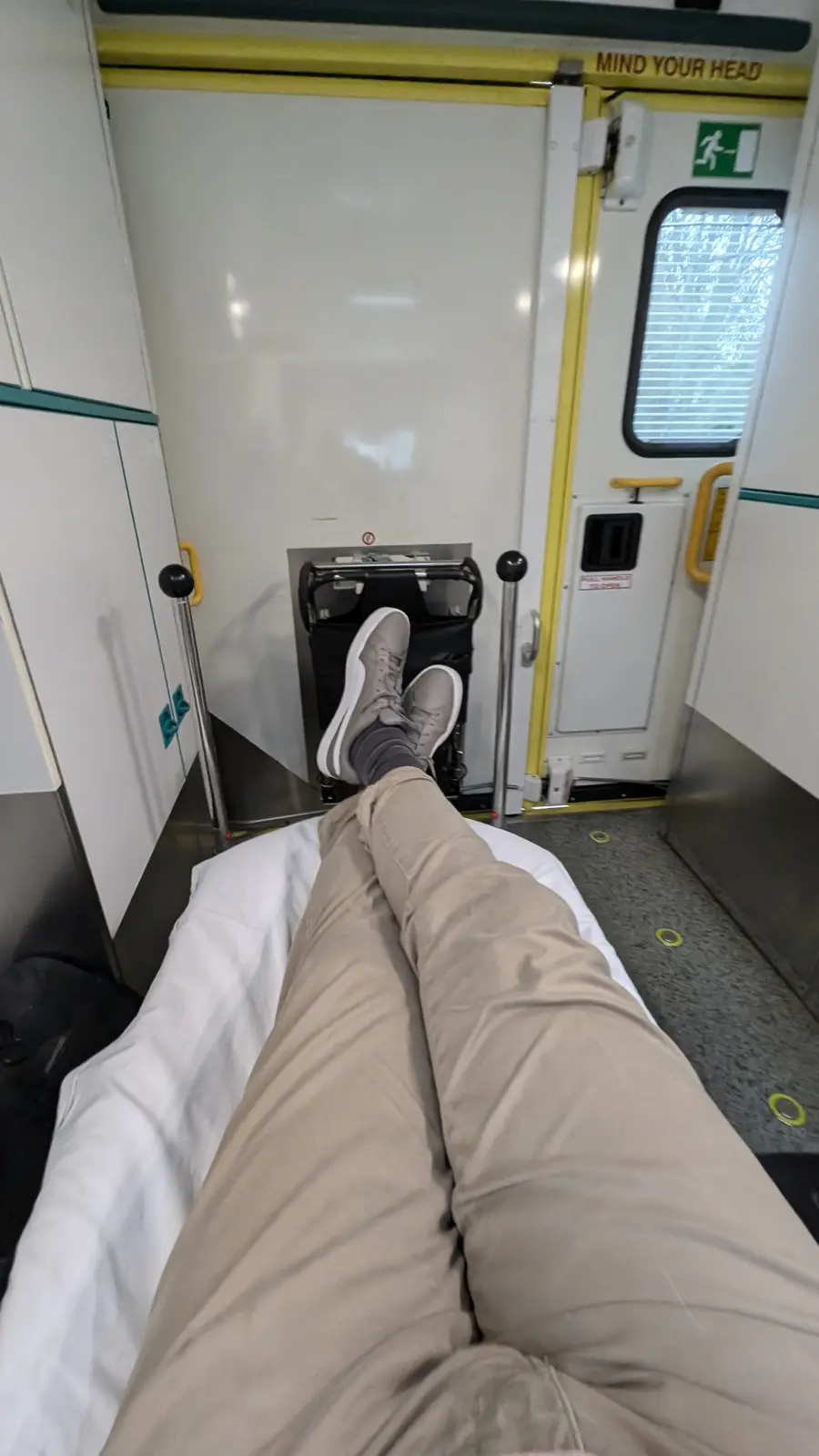 A first-person view from someone lying down on a train seat with their feet resting on a folded luggage rack, directly under…