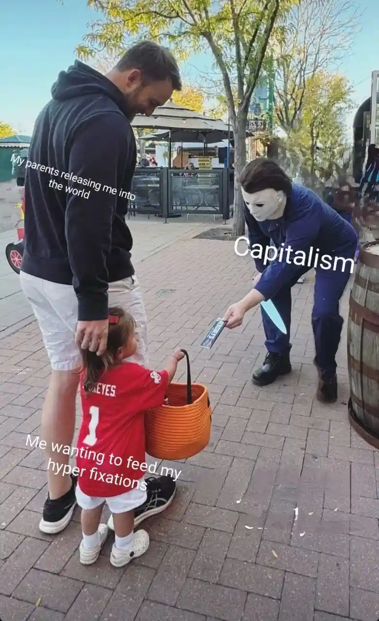 A man and a small child in a red jersey stand on a sidewalk, the child holding an orange basket. A person in a Michael Myers…