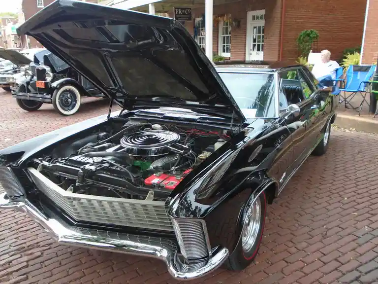 A black classic car with its hood open, revealing an engine bay that has been humorously modified to include a black…