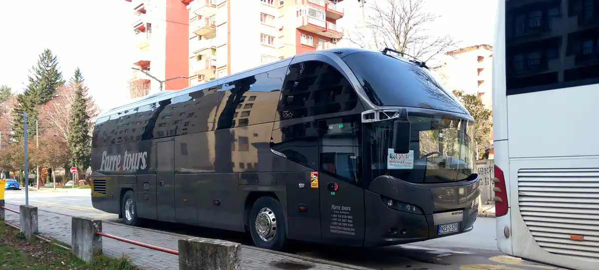 A glossy black tour bus with 'Farre tours' written on its side is parked on a city street next to a white bus. The black bus…