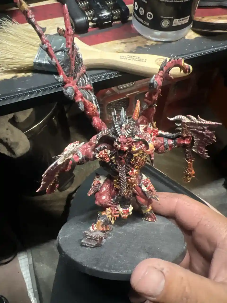A hand holds up a highly detailed, intricately painted miniature of a demonic warlord with multiple arms, horns, and wings…