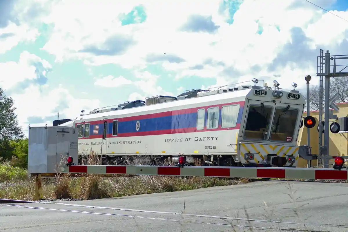 A Federal Railroad Administration train labeled 'Office of Safety' is stopped at a railroad crossing with a lowered barrier…
