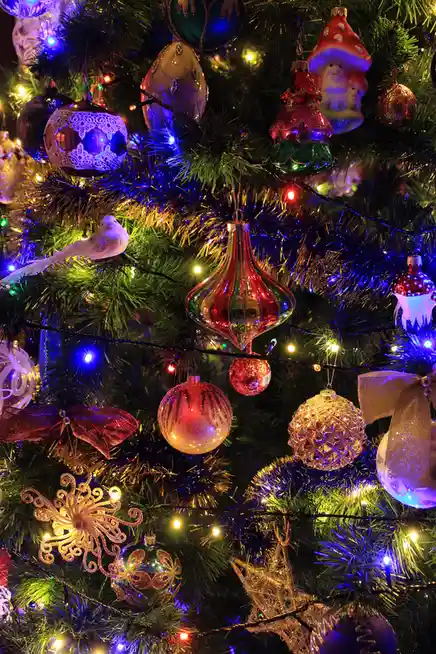 A close-up of a densely decorated artificial Christmas tree with green needles, colorful string lights (blue, red, yellow)…