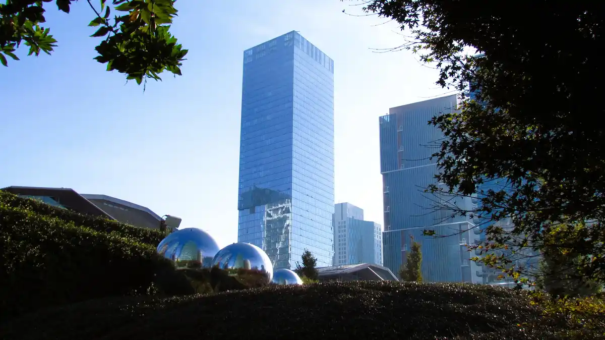 A low-angle photo shows several large, shiny chrome spheres in a landscaped area with hedges and trees framing the shot…
