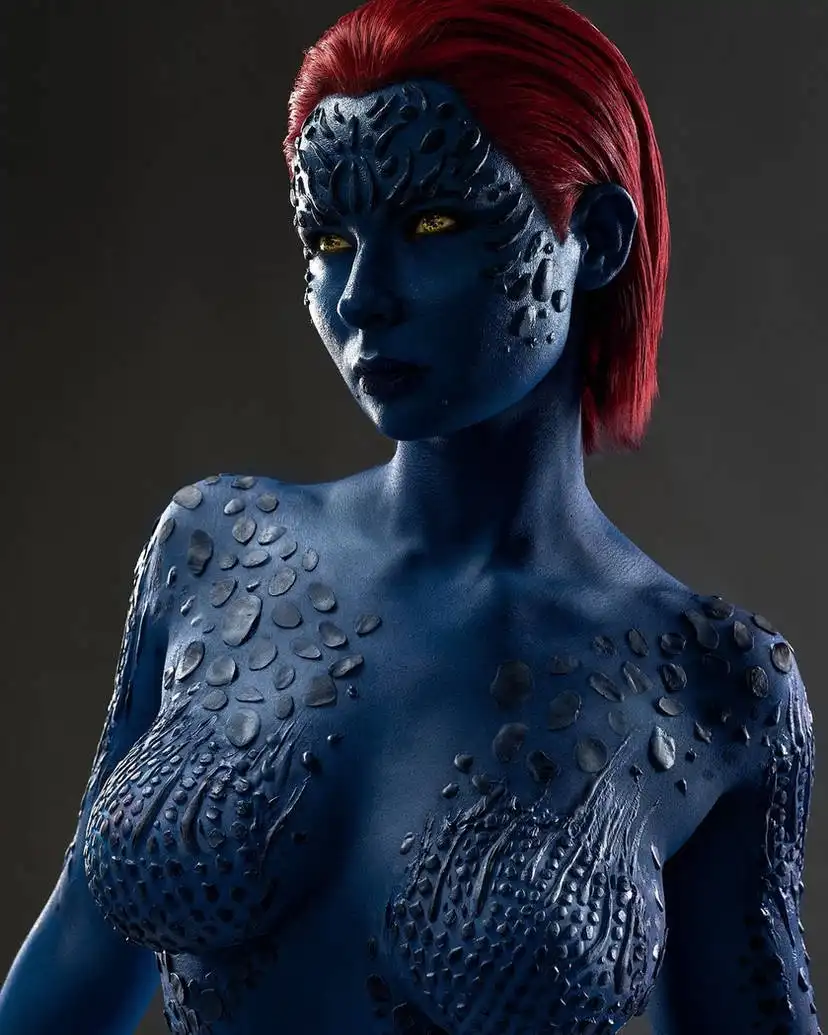 A person with blue skin, red hair, and textured, scale-like patterns across their face and torso poses against a dark…